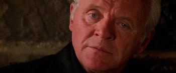 Movie still from “Mission: Impossible II” (2000), directed by John Woo – An older man with grey hair and blue eyes looking at the camera; Close Up shot, Low angle