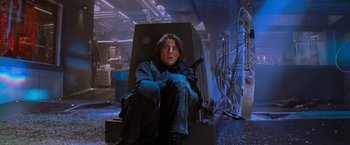 Movie still from “Mission: Impossible II” (2000), directed by John Woo – A man sitting on a chair in a room; Medium shot, Low angle