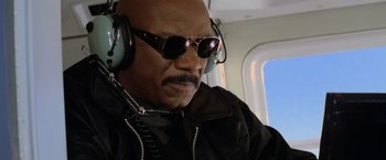 Movie still from “Mission: Impossible II” (2000), directed by John Woo – An older man wearing sunglasses and ear muffs on a plane; Close Up shot, Low angle