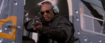 Movie still from “Mission: Impossible II” (2000), directed by John Woo – A man with a gun wearing ear muffs and sunglasses; Medium shot, Low angle