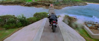 Movie still from “Mission: Impossible II” (2000), directed by John Woo – A man riding a motorcycle down a bridge over a river; Extreme Wide shot, High angle