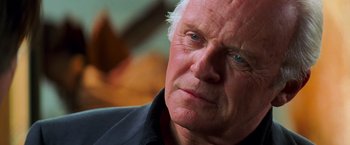 Movie still from “Mission: Impossible II” (2000), directed by John Woo – An older man with a goatee looking to his left; Close Up shot, Over the shoulder angle