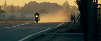 Movie still from “Mission: Impossible III” (2006), directed by J.J. Abrams – A man riding a motorcycle down the middle of a street; Wide shot, Low angle