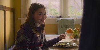 Movie still from “Mixtape” (2021), directed by Valerie Weiss – A girl sitting at a table with a bowl of fruit; Medium shot, Over the shoulder angle