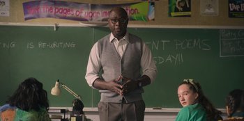 Movie still from “Mixtape” (2021), directed by Valerie Weiss – A man standing in front of a chalkboard in a classroom; Medium shot, Low angle
