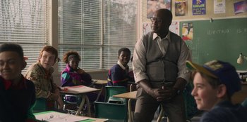 Movie still from “Mixtape” (2021), directed by Valerie Weiss – An older man standing in a classroom next to two young girls; Medium shot, Over the shoulder angle