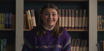 Movie still from “Mixtape” (2021), directed by Valerie Weiss – A girl in a purple sweater in front of a book shelf; Medium shot, Low angle