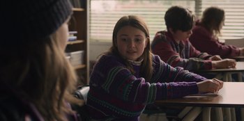 Movie still from “Mixtape” (2021), directed by Valerie Weiss – A young girl sitting at a table in front of a book shelf; Medium shot, Over the shoulder angle