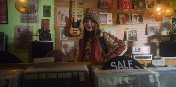 Movie still from “Mixtape” (2021), directed by Valerie Weiss – A young girl standing behind a counter in a store; Medium shot, Over the shoulder angle