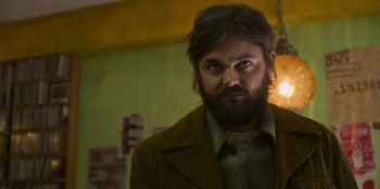 Movie still from “Mixtape” (2021), directed by Valerie Weiss – A man with long hair and a goatee stares at the camera; Medium shot, Low angle