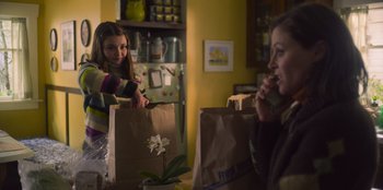 Movie still from “Mixtape” (2021), directed by Valerie Weiss – Two women are holding brown paper bags in a kitchen; Medium shot, Over the shoulder angle