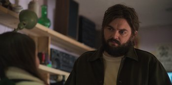 Movie still from “Mixtape” (2021), directed by Valerie Weiss – A man with a beard is standing in front of a shelf; Close Up shot, Low angle