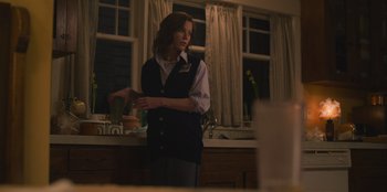 Movie still from “Mixtape” (2021), directed by Valerie Weiss – A woman standing in a kitchen holding her hands out; Medium shot, Over the shoulder angle