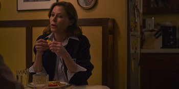 Movie still from “Mixtape” (2021), directed by Valerie Weiss – A woman sitting at a table eating a piece of food; Medium shot, Over the shoulder angle