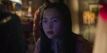 Movie still from “Mixtape” (2021), directed by Valerie Weiss – A young girl wearing glasses looking at the camera; Close Up shot, Over the shoulder angle