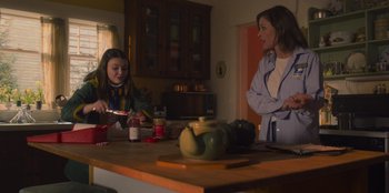 Movie still from “Mixtape” (2021), directed by Valerie Weiss – Two women sitting at a kitchen table talking to each other; Medium shot, Over the shoulder angle