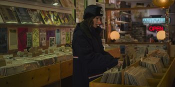Movie still from “Mixtape” (2021), directed by Valerie Weiss – A woman is looking through a shelf of records in a store; Medium shot, High angle