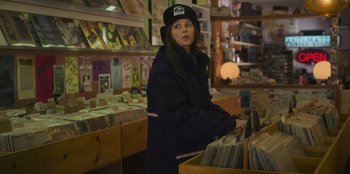 Movie still from “Mixtape” (2021), directed by Valerie Weiss – A woman standing in front of a record store; Medium shot, Over the shoulder angle