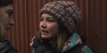 Movie still from “Mixtape” (2021), directed by Valerie Weiss – A young woman wearing a colorful knitted hat; Close Up shot, Over the shoulder angle