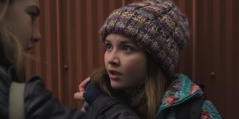 Movie still from “Mixtape” (2021), directed by Valerie Weiss – A young woman wearing a colorful hat and jacket; Close Up shot, Over the shoulder angle