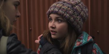 Movie still from “Mixtape” (2021), directed by Valerie Weiss – A young girl wearing a colorful hat and jacket; Close Up shot, Over the shoulder angle