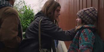 Movie still from “Mixtape” (2021), directed by Valerie Weiss – A man with long brown hair is touching a woman's face; Medium shot, Low angle