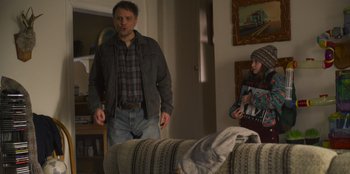 Movie still from “Mixtape” (2021), directed by Valerie Weiss – A man and a woman standing in front of a couch; Medium shot, Over the shoulder angle