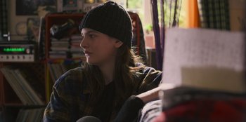 Movie still from “Mixtape” (2021), directed by Valerie Weiss – A woman sitting on a couch wearing a hat; Close Up shot, Over the shoulder angle