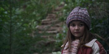 Movie still from “Mixtape” (2021), directed by Valerie Weiss – A young girl wearing a hat and a scarf; Close Up shot, High angle