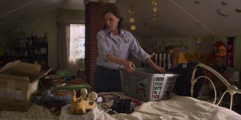 Movie still from “Mixtape” (2021), directed by Valerie Weiss – A woman holding a laundry basket in a room; Medium shot, Low angle