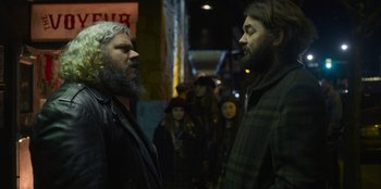 Movie still from “Mixtape” (2021), directed by Valerie Weiss – Two bearded men standing next to each other on the street; Medium shot, Over the shoulder angle