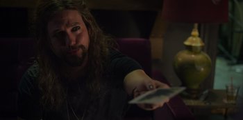 Movie still from “Mixtape” (2021), directed by Valerie Weiss – A man with long hair is holding a remote control; Close Up shot, Over the shoulder angle
