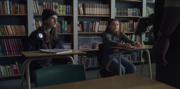 Movie still from “Mixtape” (2021), directed by Valerie Weiss – Two women sitting at a table in front of bookshelves; Medium shot, Low angle