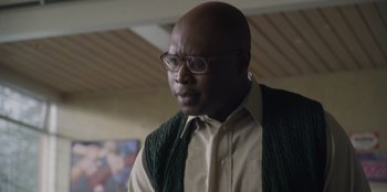 Movie still from “Mixtape” (2021), directed by Valerie Weiss – A bald man wearing glasses and a green sweater vest; Close Up shot, Low angle
