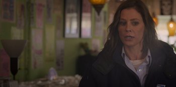 Movie still from “Mixtape” (2021), directed by Valerie Weiss – A woman standing in front of a table with papers on it; Close Up shot, Over the shoulder angle