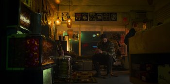 Movie still from “Mixtape” (2021), directed by Valerie Weiss – A man sitting on a chair looking at his cell phone; Wide shot, Low angle