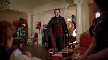 Movie still from “Monster High 2” (2023), directed by Todd Holland – A man dressed as a vampire standing in front of a table; Medium shot, Over the shoulder angle