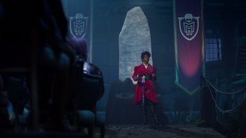 Movie still from “Monster High 2” (2023), directed by Todd Holland – A man in a red coat standing in front of a stone wall; Wide shot, Over the shoulder angle