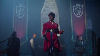 Movie still from “Monster High 2” (2023), directed by Todd Holland – A woman in a red coat standing in front of a large stone; Wide shot, Over the shoulder angle