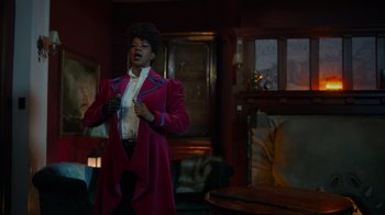 Movie still from “Monster High 2” (2023), directed by Todd Holland – A woman in a pink coat standing in front of a window; Medium shot, Over the shoulder angle