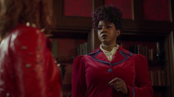 Movie still from “Monster High 2” (2023), directed by Todd Holland – A woman in a red jacket is standing in front of a mirror; Medium shot, Over the shoulder angle