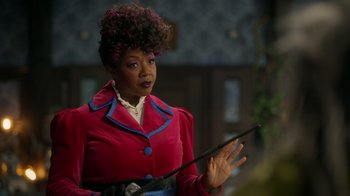 Movie still from “Monster High 2” (2023), directed by Todd Holland – A woman in a red coat holding a wand in her hand; Medium shot, Over the shoulder angle