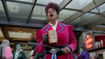 Movie still from “Monster High 2” (2023), directed by Todd Holland – A woman dressed in a pink outfit holding a cup; Medium shot, Low angle