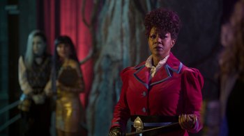 Movie still from “Monster High 2” (2023), directed by Todd Holland – A woman in a red jacket holding a sword in front of another woman in a gold dress; Medium shot, Over the shoulder angle