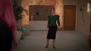Movie still from “Monster High 2” (2023), directed by Todd Holland – A woman in a green jacket and black skirt standing in a living room; Wide shot, Low angle