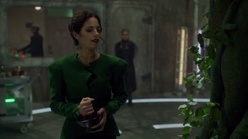 Movie still from “Monster High 2” (2023), directed by Todd Holland – A woman in a green jacket standing next to a plant; Medium shot, Over the shoulder angle