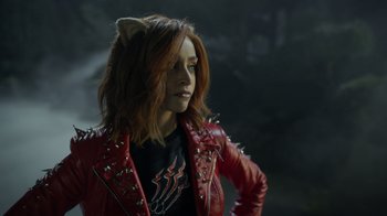 Movie still from “Monster High 2” (2023), directed by Todd Holland – A woman in a red leather jacket with a cat on it's head; Medium shot, Over the shoulder angle