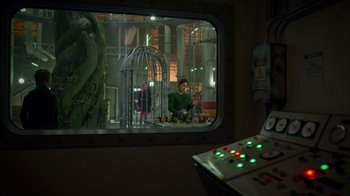 Movie still from “Monster High 2” (2023), directed by Todd Holland – A man in green shirt sitting in front of a bird cage; Medium shot, Over the shoulder angle