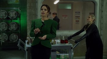 Movie still from “Monster High 2” (2023), directed by Todd Holland – A woman in a green jacket standing in front of a counter; Medium shot, Over the shoulder angle