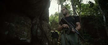 Movie still from “Monsters of Man” (2020), directed by Mark Toia – A man holding a gun while standing next to a tree; Medium shot, Low angle
